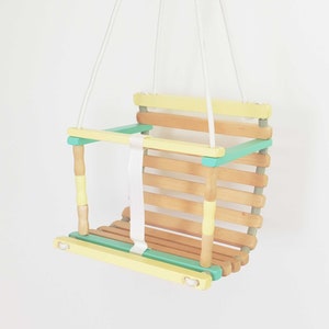 Wooden baby swing part natural wood, part painted in pale yellow and light green colors.