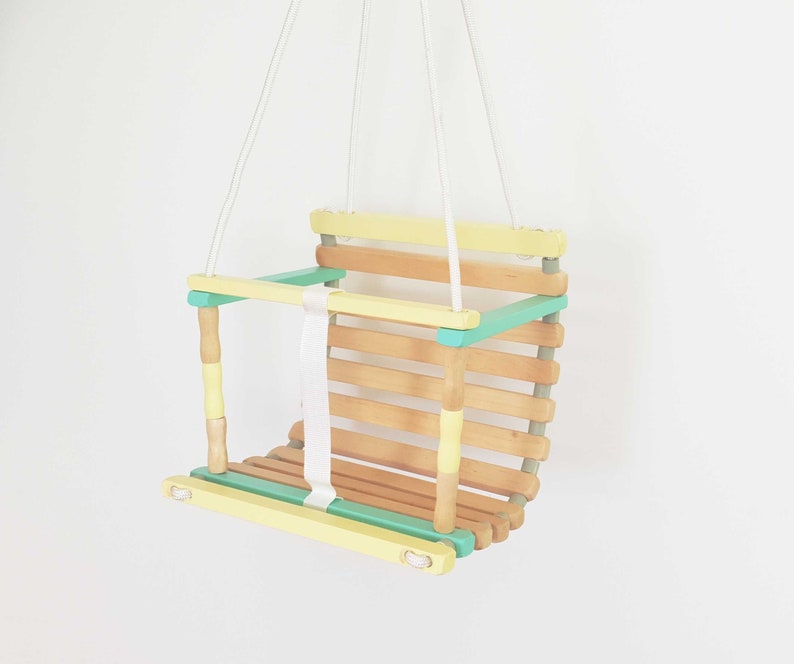 Wooden baby swing part natural wood, part painted in pale yellow and light green colors.