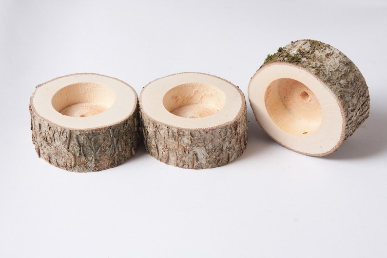 Pu&ograve; includere: Tre portacandele in legno realizzati in corteccia d'albero con una finitura in legno naturale. I portacandele sono rotondi e hanno un centro vuoto.