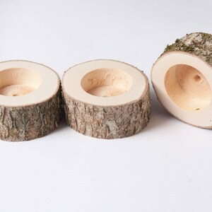 Puede incluir: Tres portavelas de madera hechos de corteza de &aacute;rbol con un acabado de madera natural. Los portavelas son redondos y tienen un centro hueco.