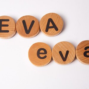 K&ouml;nnte beinhalten: Holzbrettchen mit Buchstaben, die den Namen "EVA" in Gro&szlig;buchstaben und "eva" in Kleinbuchstaben buchstabieren.