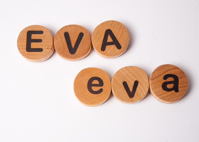 K&ouml;nnte beinhalten: Holzbrettchen mit Buchstaben, die den Namen "EVA" in Gro&szlig;buchstaben und "eva" in Kleinbuchstaben buchstabieren.