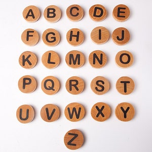 K&ouml;nnte beinhalten: Holzalphatile mit schwarzen Buchstaben auf wei&szlig;em Hintergrund. Die Kacheln sind in alphabetischer Reihenfolge von A bis Z angeordnet.