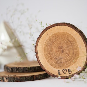 Peut inclure: Trois sous-verres en bois avec des bords en écorce naturelle. Le sous-verre du haut porte les initiales "L♥B" gravées dans le bois.