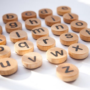 K&ouml;nnte beinhalten: Holzbrettchen mit Buchstaben des Alphabets in schwarzer Schrift. Die Brettchen sind in einem Halbkreis auf einer wei&szlig;en Oberfl&auml;che angeordnet.
