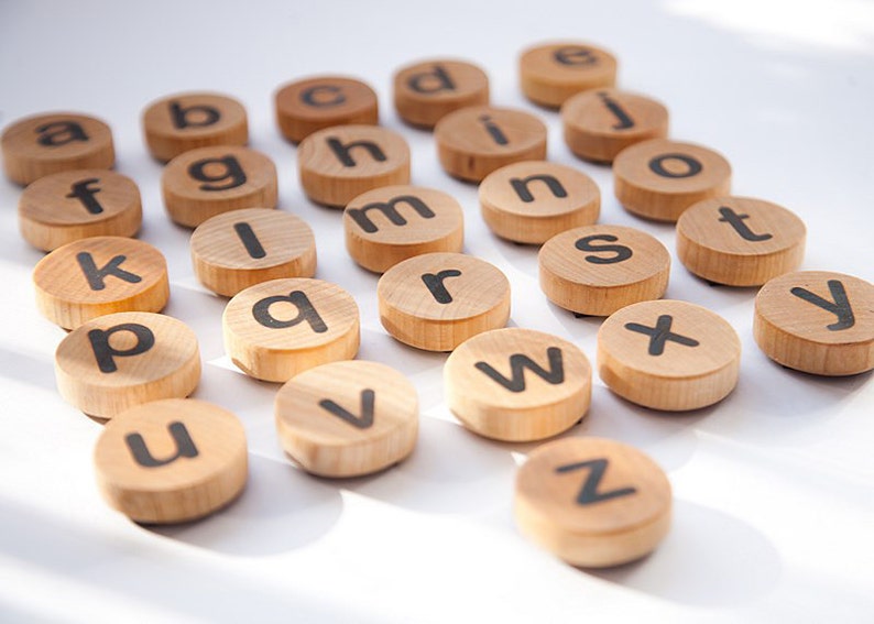 K&ouml;nnte beinhalten: Holzbrettchen mit Buchstaben des Alphabets in schwarzer Schrift. Die Brettchen sind in einem Halbkreis auf einer wei&szlig;en Oberfl&auml;che angeordnet.