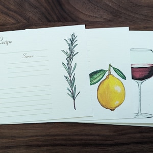 May include: A set of recipe cards with a blank recipe card, a card with a sprig of rosemary, a card with a lemon, a card with a glass of red wine, and a card with a loaf of bread.
