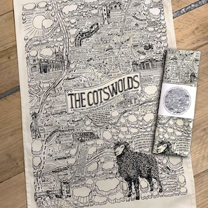 May include: A black and white illustration of a map of The Cotswolds, a region in England. The map is filled with details of towns, villages, and landmarks. The text "The Cotswolds" is written in a large font at the top of the map. A black sheep is in the bottom right corner of the map.