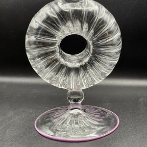 Puede incluir: Un jarrón de vidrio transparente con forma de donut y superficie texturizada. El jarrón tiene una base redonda con un borde rosa.