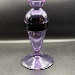 May include: A purple glass vase with a wide base and a narrow neck. The vase has a dark band around the middle.