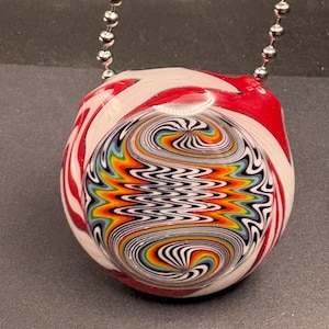 May include: A colorful glass pendant necklace with a swirling design. The pendant features a mix of red, white, yellow, orange, blue, and black colors. The necklace has a silver ball chain.