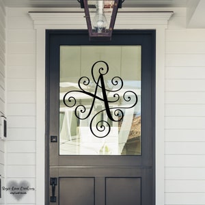 May include: A black vinyl decal of a stylized letter A with decorative swirls, applied to a glass front door.