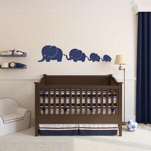 Peut inclure: Un lit b&eacute;b&eacute; en bois brun avec un matelas ray&eacute; blanc et bleu marine et une jupe ray&eacute;e bleu marine et blanche. Le lit b&eacute;b&eacute; est dans une chambre d'enfant avec un mur blanc et un rideau bleu. Il y a quatre silhouettes d'&eacute;l&eacute;phants bleu marine sur le mur.
