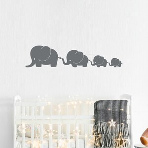 Peut inclure: Un autocollant mural de cr&egrave;che repr&eacute;sentant une ligne de quatre &eacute;l&eacute;phants gris de tailles diff&eacute;rentes, chacun avec une trompe lev&eacute;e et reli&eacute;e &agrave; la queue de l'&eacute;l&eacute;phant suivant. Les &eacute;l&eacute;phants sont dispos&eacute;s en ligne du plus grand au plus petit, cr&eacute;ant un design ludique et fantaisiste.