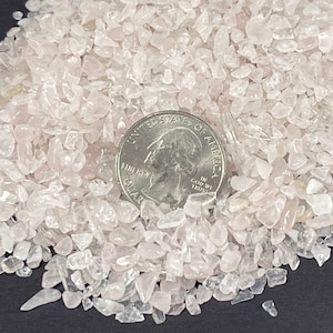 May include: A pile of small, clear, and translucent rose quartz chips. The chips are about the size of a US quarter.