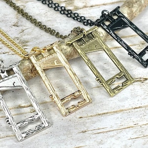 May include: Four guillotine pendant necklaces in different metal finishes: silver, gold, bronze, and black. Each pendant features a detailed design of a guillotine with a textured woodgrain effect.