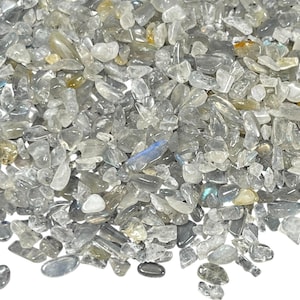May include: A close-up view of a pile of small, irregularly shaped, translucent gemstones. The stones are primarily gray with hints of blue, yellow, and brown. The gemstones are scattered across the frame.
