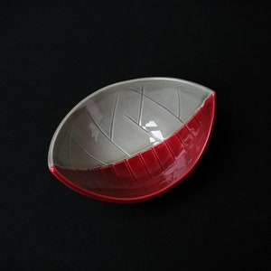 Puede incluir: Un pequeño cuenco de cerámica con un diseño gris y rojo. El cuenco tiene forma de hoja y una superficie texturizada.