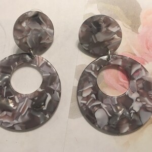 May include: A pair of dangle earrings with a gray and white marbled pattern. The earrings are made of two circles, one smaller than the other. The smaller circle sits on top of the larger circle.