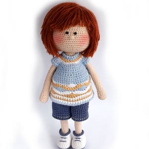 May include: A crocheted doll with red hair, a blue and white striped shirt, blue shorts, and white sneakers.