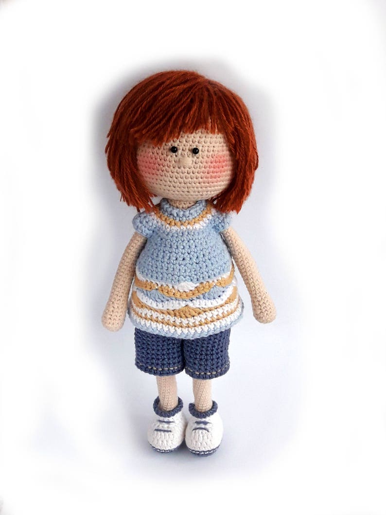 May include: A crocheted doll with red hair, a blue and white striped shirt, blue shorts, and white sneakers.
