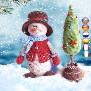 Puede incluir: Un muñeco de nieve de crochet que lleva un chaleco rojo, una bufanda azul y un sombrero marrón, de pie junto a un árbol de Navidad verde de crochet con botones rojos y azules. El muñeco de nieve y el árbol están sobre un fondo blanco nevado.