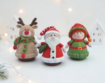 May include: Three crocheted figurines featuring a tan reindeer with a red nose and green scarf, a Santa Claus in a red and white suit with a beard, and an elf in a green outfit with a red hat, all crafted with detailed yarn stitching.