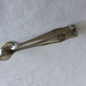 May include: Silver sugar tongs with an ornate design and the inscription "1883" on the handle.