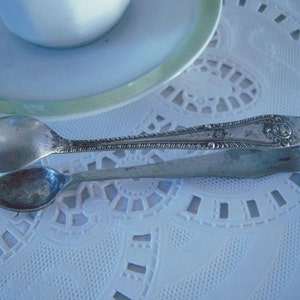 May include: Silver sugar tongs with an ornate design. The tongs are on a white lace tablecloth.