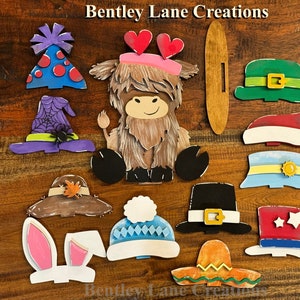 May include: A set of 12 wooden cutout hat shapes, painted in various colors and designs. The hats include a witch hat, a cowboy hat, a bunny ear headband, a Santa hat, a sombrero, a pilgrim hat, a winter hat, a party hat, a leprechaun hat, a  hat with a sun and a yellow band, and a top hat. The hats are all approximately 4 inches in diameter.