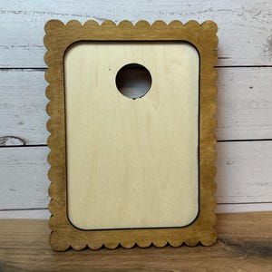 May include: A rectangular wooden frame with a scalloped edge and a light-colored center panel. The frame features a dark brown stained finish on the outer border and a circular cutout near the top center of the light-colored interior panel.