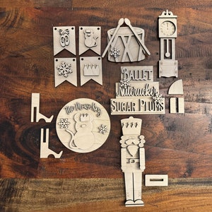 May include: Wooden craft kit featuring a Nutcracker, Mouse King, and other characters from the ballet The Nutcracker. The kit includes a clock, drum, and banners with snowflakes, crowns, and ballet shoes.