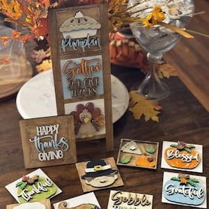 May include: A collection of wooden Thanksgiving themed signs with various designs and phrases, including "Pumpkin", "Gather and Give Thanks", "Happy Thanks Giving", "Thankful", "Gobble Til You Wobble", "Blessed", and "Grateful".