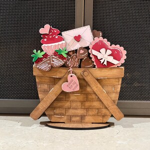 May include: Wooden basket decoration filled with Valentine's Day treats. Includes a cupcake, chocolate-covered strawberries, heart-shaped chocolates, and a heart-shaped gift box. A pink heart-shaped tag reads "Sweets for my sweet."