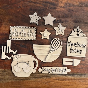 May include: Wooden Christmas cookie decorating kit with a Santa Claus, a bowl, a whisk, a rolling pin, a cookie jar, and stars. The rolling pin says "Baking Spirits Bright". The cookie jar says "Christmas Cookies".