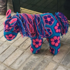 Könnte beinhalten: Ein gehäkeltes Pferdespielzeug mit einem rosa-blauen Blumenmuster. Das Pferd hat eine lange, rosa-blaue Mähne und einen Schwanz.