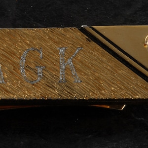 Puede incluir: Pinza para billetes de oro con un diamante y las iniciales "AGK" grabadas en la parte delantera.