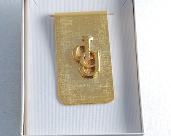 May include: A gold money clip with the letters "JG" embossed on the front. The clip is in a white box with a gold trim.