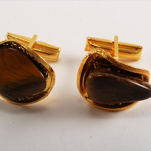 May include: A pair of gold cufflinks with brown tiger's eye stones set in a decorative gold frame.