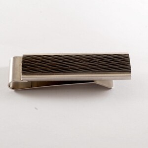 May include: A silver money clip with a rectangular, textured, dark brown centre. The clip has a curved design for holding cash or cards. A practical accessory for everyday use.