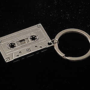 May include: A silver metal cassette tape keychain with a silver key ring.