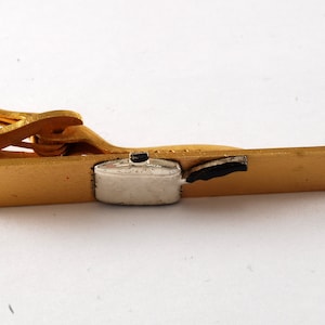 May include: Gold tie clip featuring a silver and black enamel design of a cooking pot.