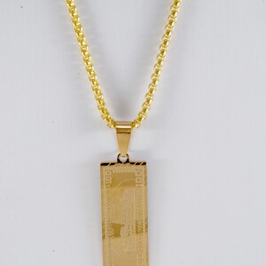 May include: A gold chain necklace with a pendant shaped like a $100 bill.