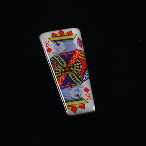 Puede incluir: Un encendedor rectangular blanco con temática de cartas de juego que presenta el Rey de Diamantes. El diseño incluye detalles rojos, azules y amarillos, con la letra "K" visible en ambos extremos. El encendedor tiene un acabado brillante.