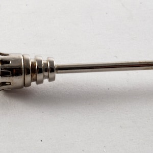 May include: A silver tie tack with a black stone set in a crown-like design.