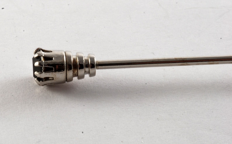 May include: A silver tie tack with a black stone set in a crown-like design.