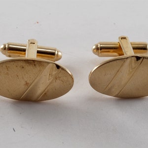 May include: A pair of gold oval cufflinks with a textured design.