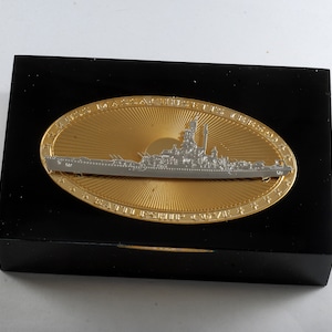 Könnte beinhalten: Eine schwarze Holzplakette mit einer goldenen ovalen Plakette, die ein silbernes Reliefbild des Schlachtschiffs USS Massachusetts zeigt. Die ovale Plakette trägt die Aufschrift "USS Massachusetts BB-59 Battleship Cover"