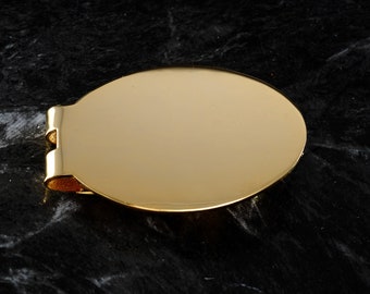 May include: A gold-colored metal money clip with a smooth, oval-shaped top. The clip is designed to hold bills together.