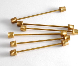 May include: A set of eight gold-toned metal hat pins with a decorative spiral design on the top. The pins are arranged in a fan shape on a white surface.